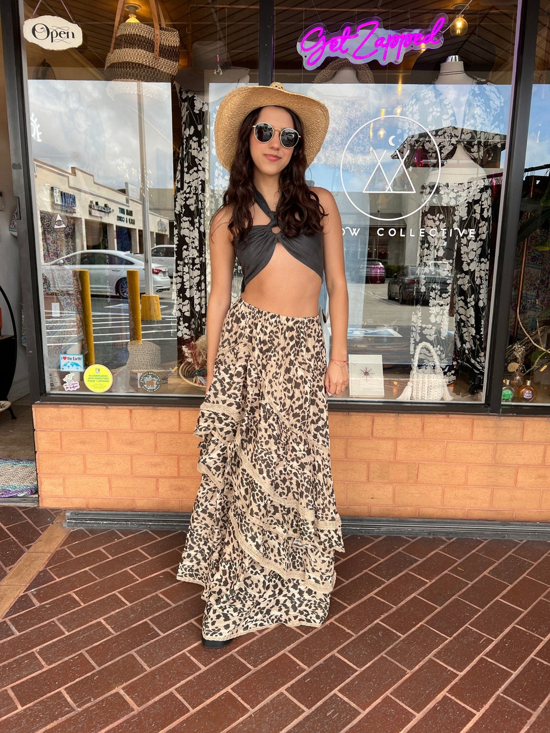 woman dressed in boho style with leopard print maxi skirt and black top, and boho cowgirl style hat.
