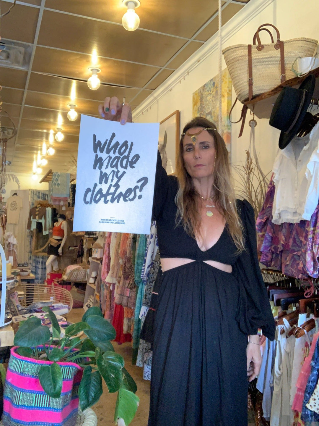 woman in black dress holding fashion revolution sign that says who made my clothes?