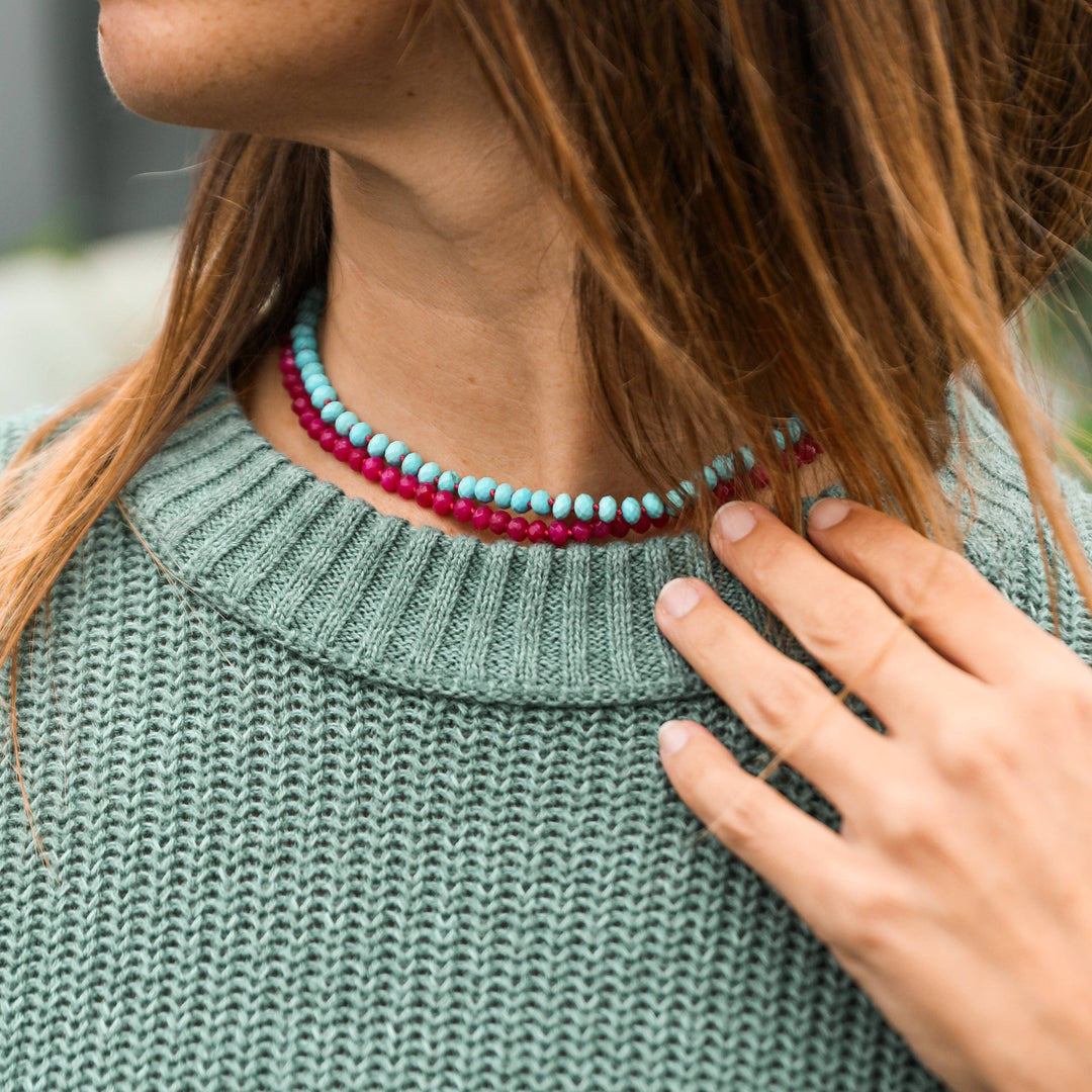 Turquoise necklace layered with a pink gemstone necklace over a knit sweater
