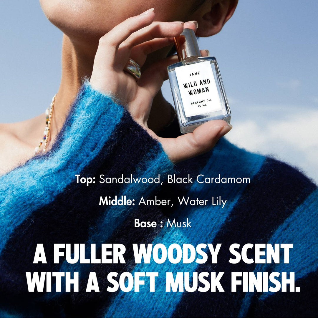 Hand holding Jane perfume oil against a blue sky with notes of sandalwood, cardamom, amber, water lily and musk