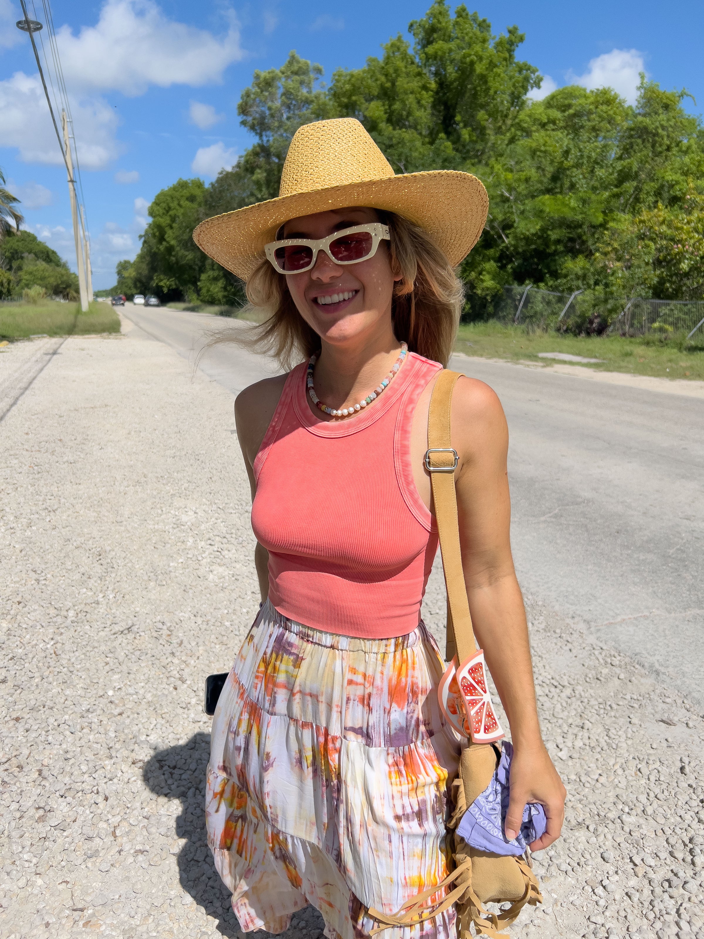 Woman in a pink top and straw hat standing on a road with trees in the background