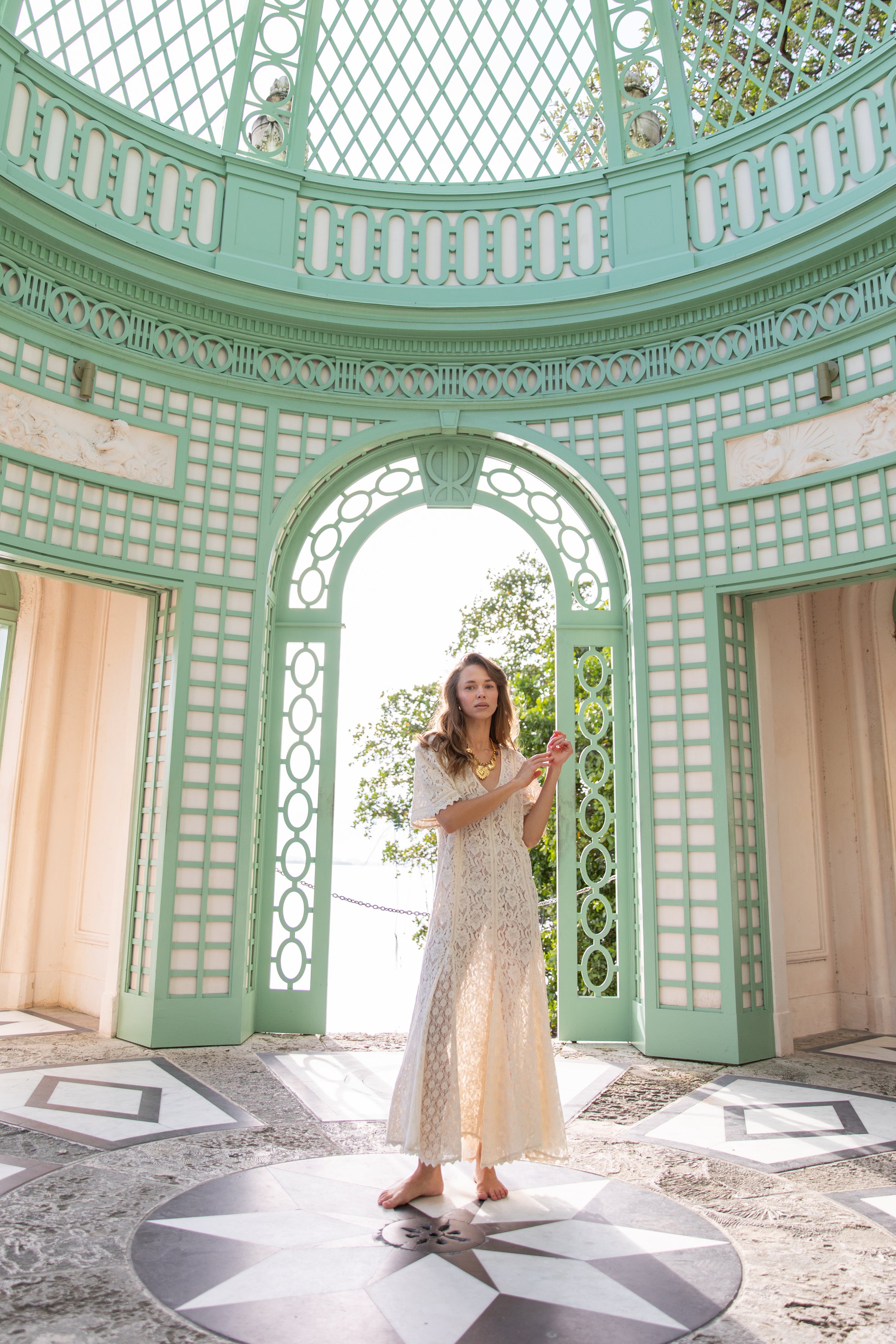Woman in a white dress standing inside a decorative green gazebo.