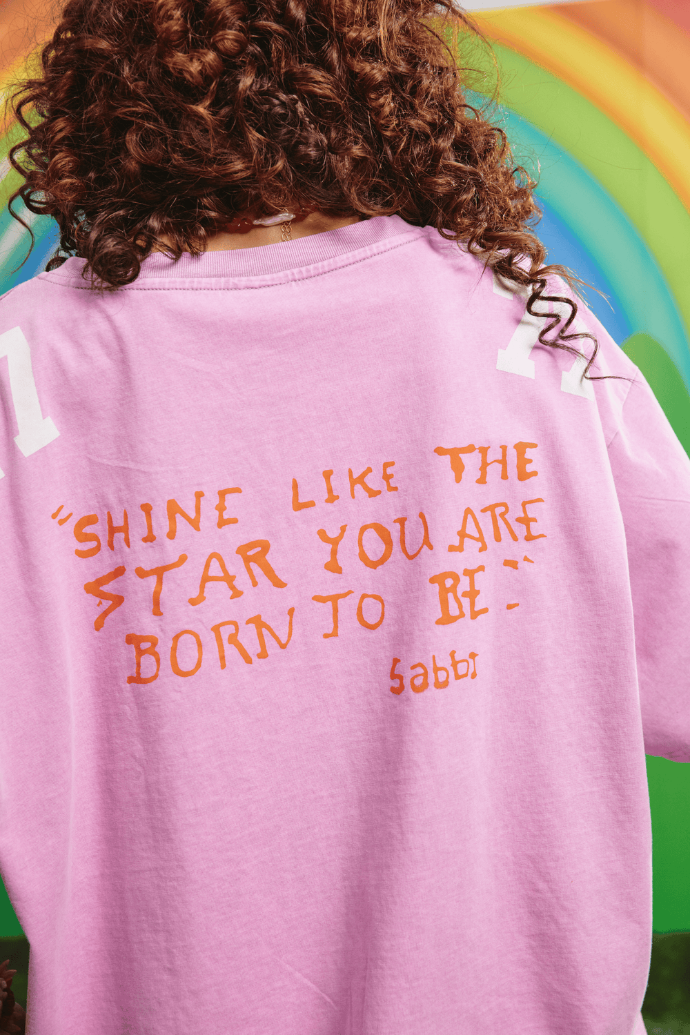 Close-up detail of the orange SABBI appliqué on the purple 77 tee