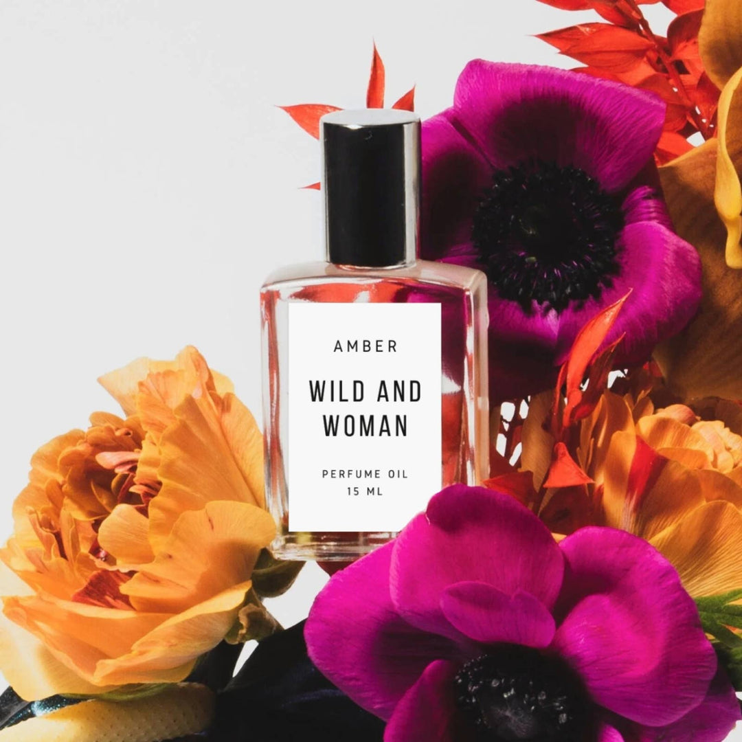 Wild and Woman Amber perfume oil bottle among orange roses and magenta anemones