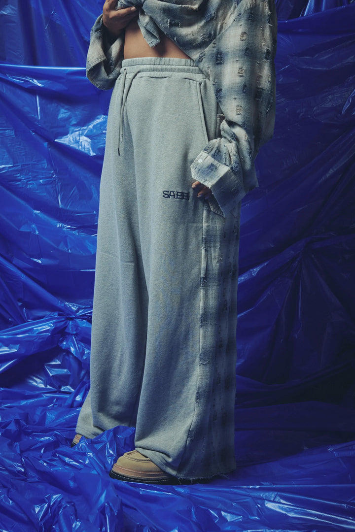 A person wearing loose light gray drawstring sweatpants with a small black &
