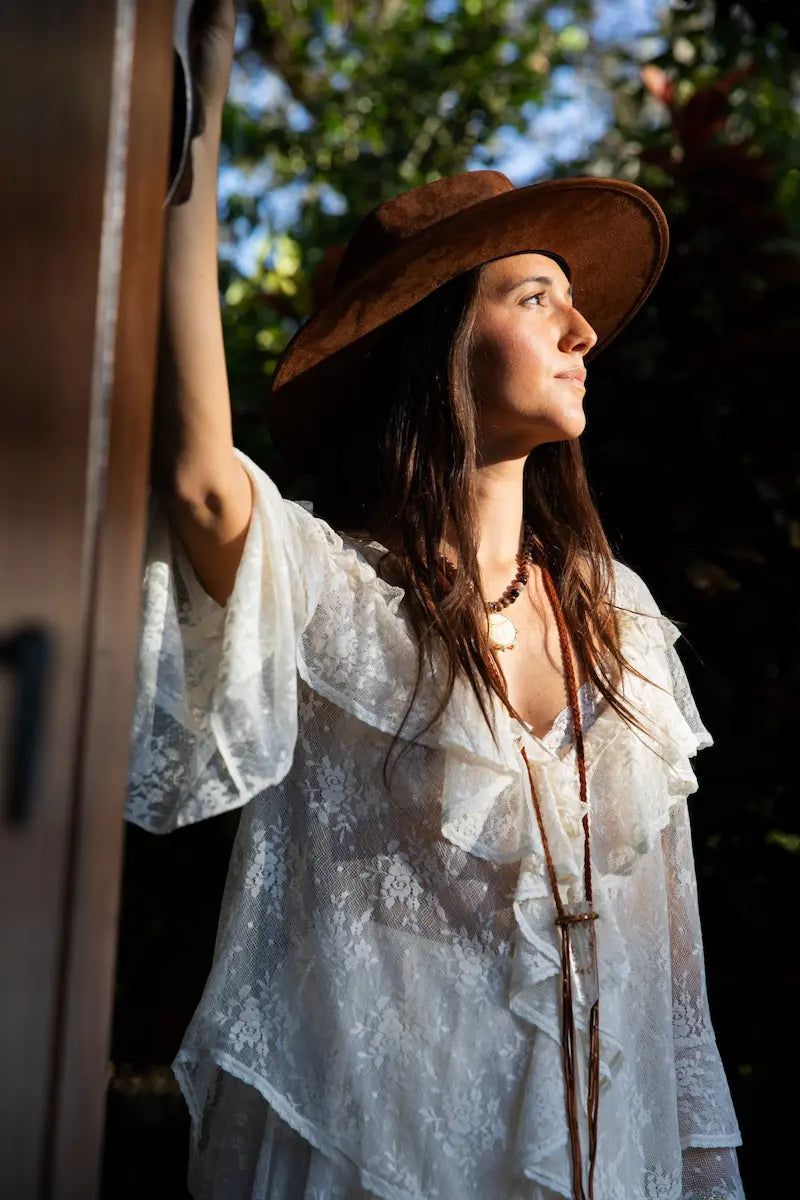 Woman wearing a white lace top and brown hat with a blurred background
