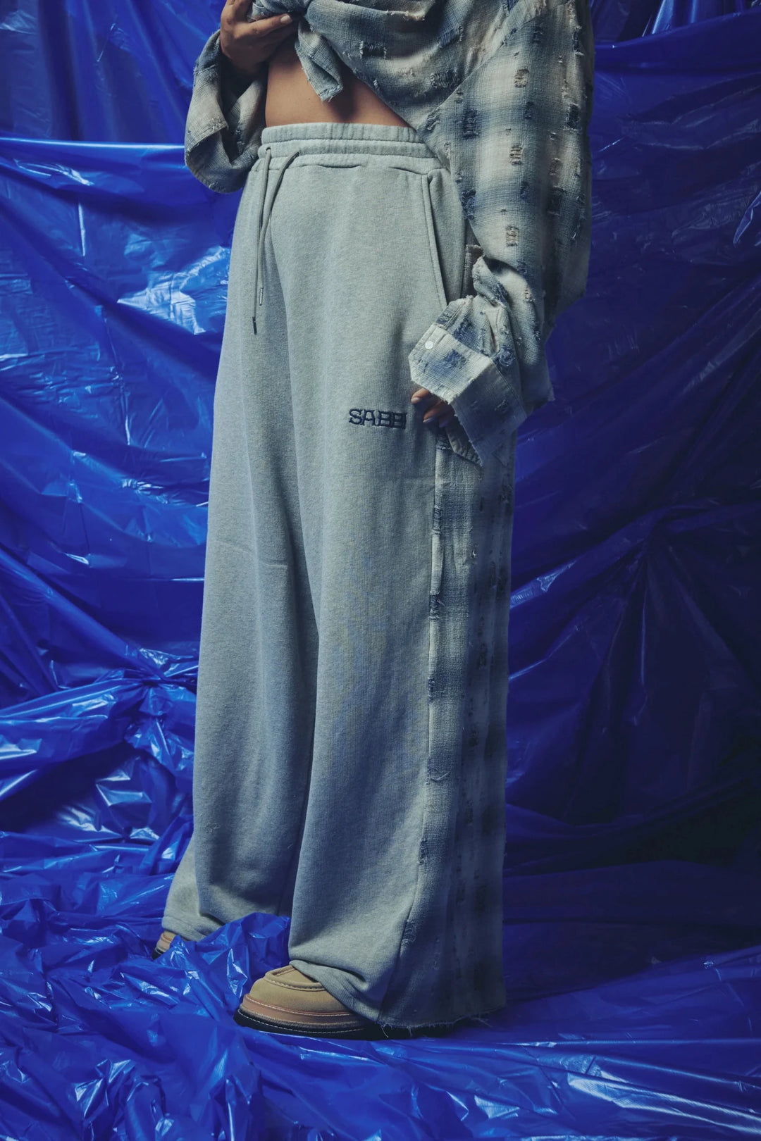 A person wearing loose light gray drawstring sweatpants with a small black &