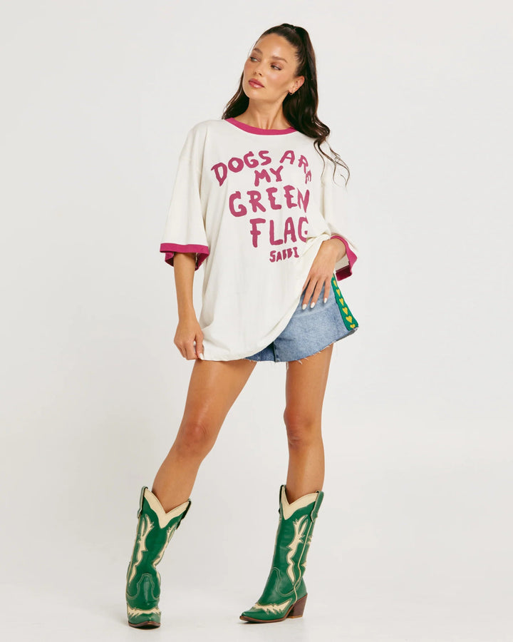 Woman wearing a white oversized shirt with text, denim skirt, and green cowboy boots on a white background