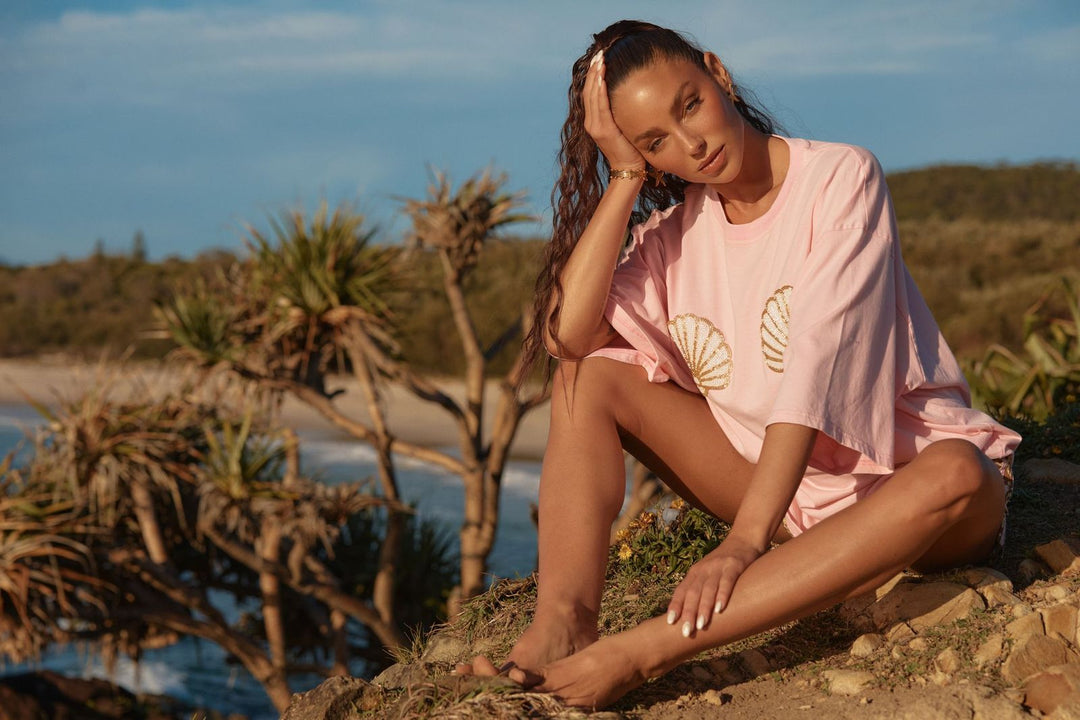 Woman in a pink oversized tee sitting on a rocky outcrop with a scenic background