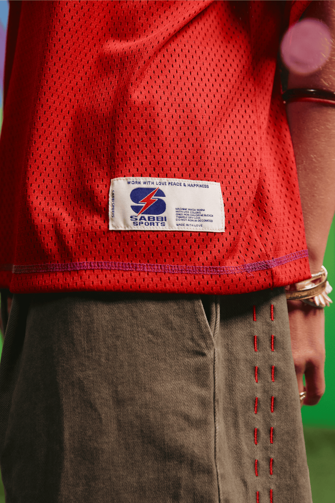 Detail of the SABBI woven hem label on the red mesh tee