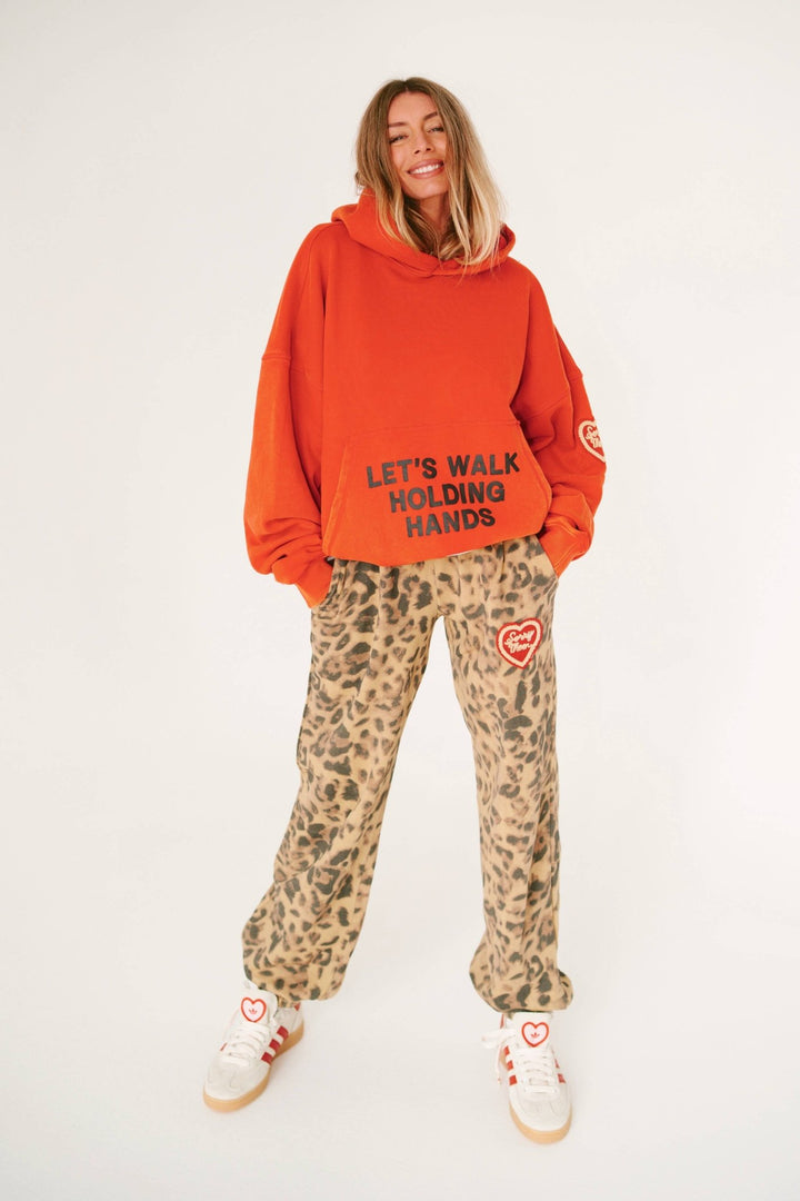 Person wearing an orange hoodie with text and leopard print pants on a white background