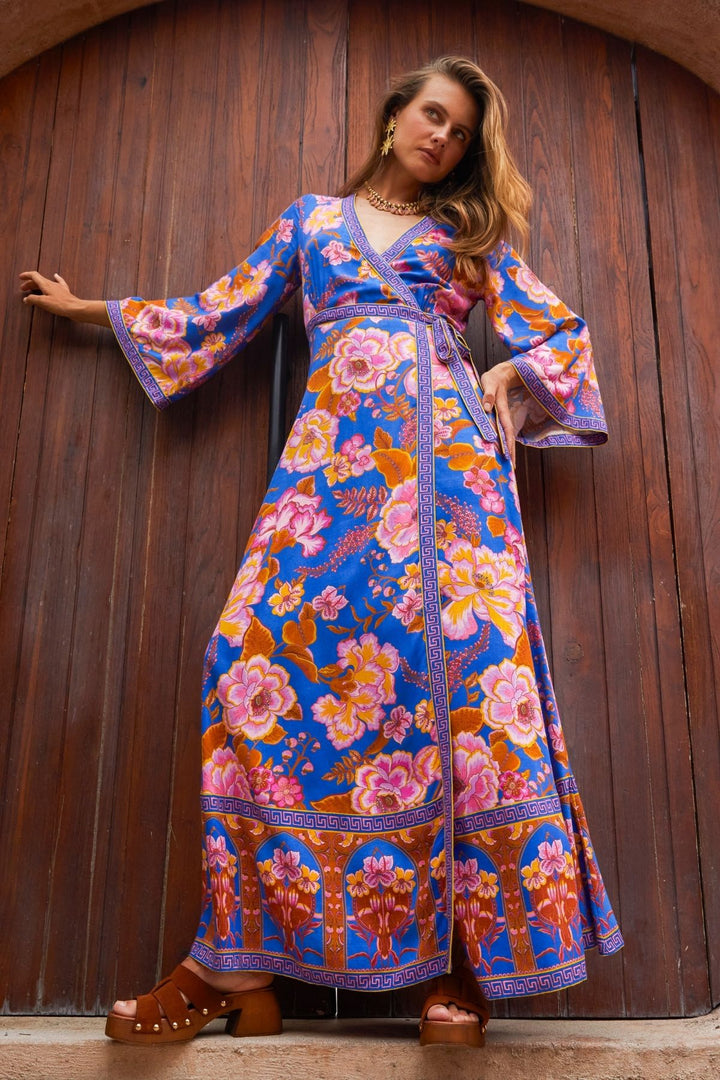 Woman wearing a colorful floral dress against a wooden wall