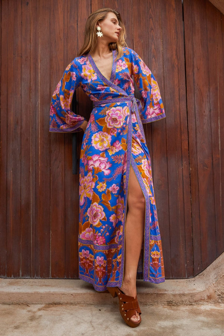 Woman wearing a colorful floral dress standing against a wooden wall.