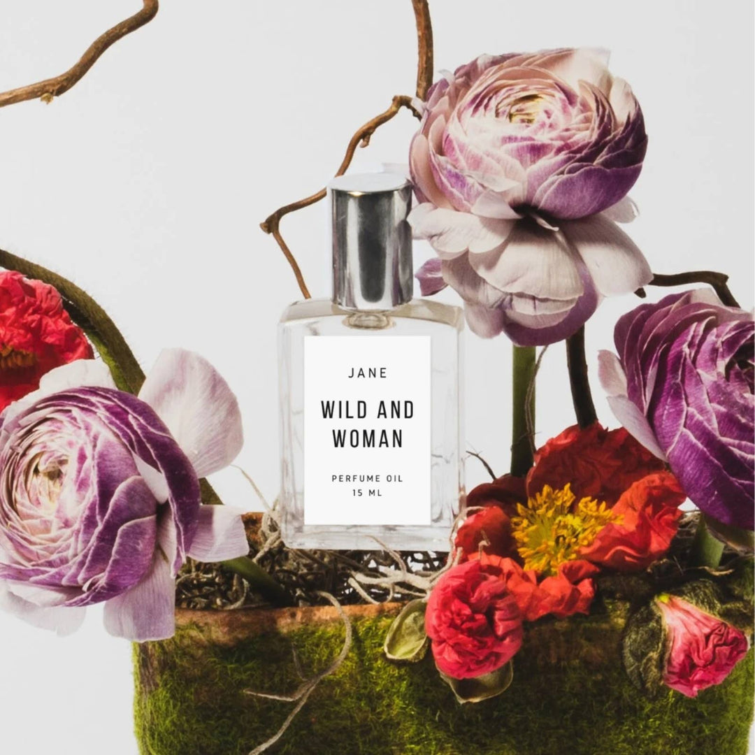 Wild and Woman Jane perfume oil among purple ranunculus and red flowers on moss