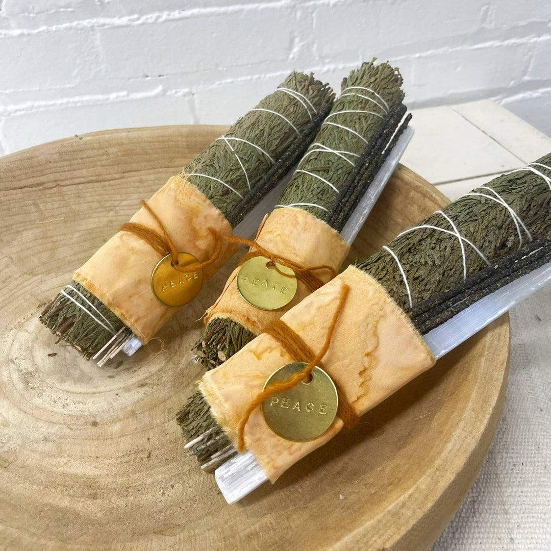 Three bundles of sage tied with ribbons on a wooden surface with a white background